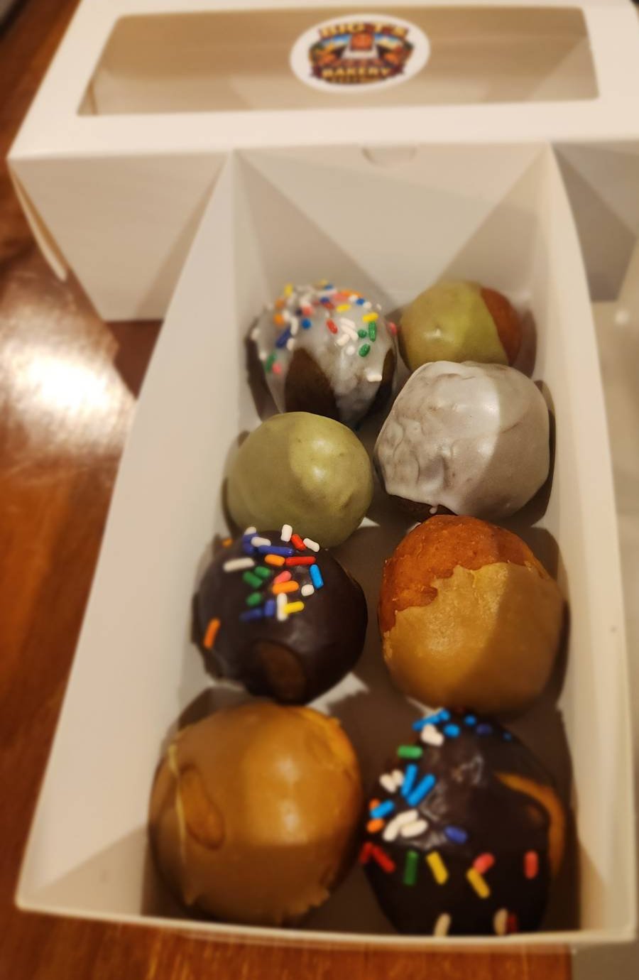 A box of assorted donut holes in glazed, matcha, and chocolate-sprinkle flavours